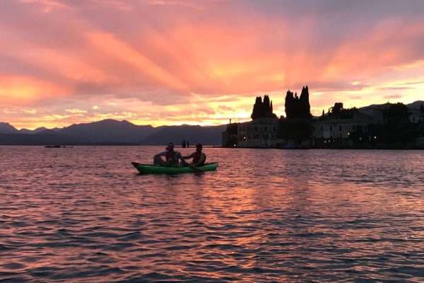 Coppia in kayak verde al tramonto sul Lago di Garda davanti a Punta San Vigilio con cipressi