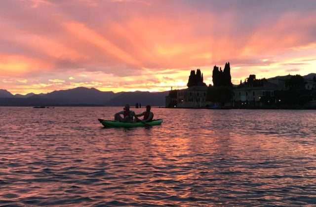 Coppia in kayak verde al tramonto sul Lago di Garda davanti a Punta San Vigilio con cipressi