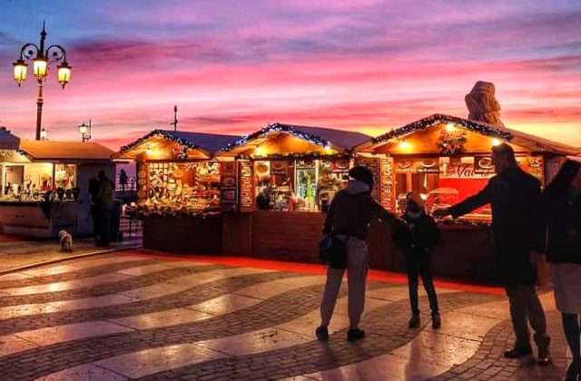 Wooden stalls of the Lazise Christmas market lit up at sunset along the lakefront