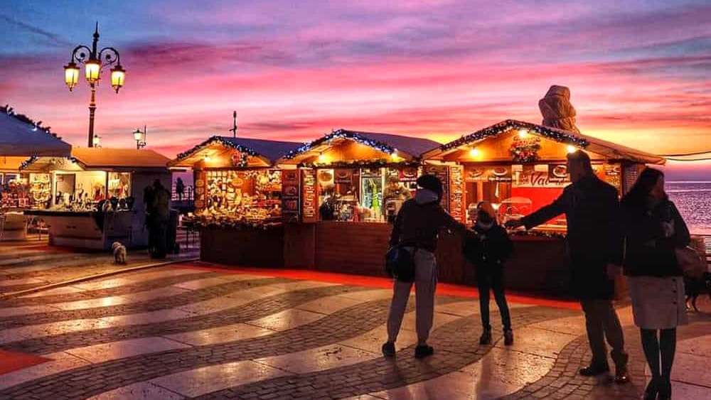 Casette in legno del mercatino di Natale di Lazise illuminate al tramonto sul lungolago