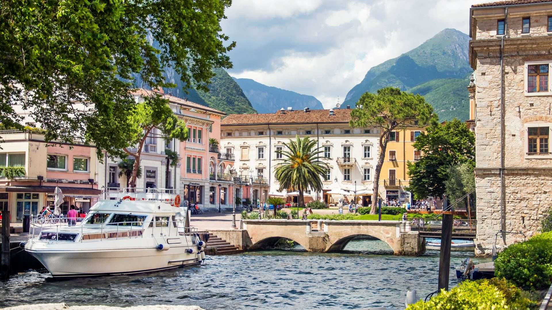 Vista del porto di Riva del Garda con barche, palme e Monte Brione sullo sfondo