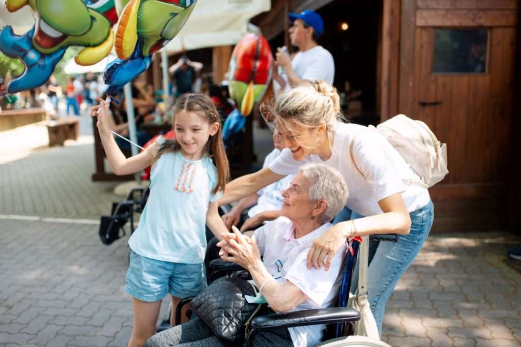 Dziewczynka z balonami, kobieta i starsza pani na wózku inwalidzkim w Gardaland