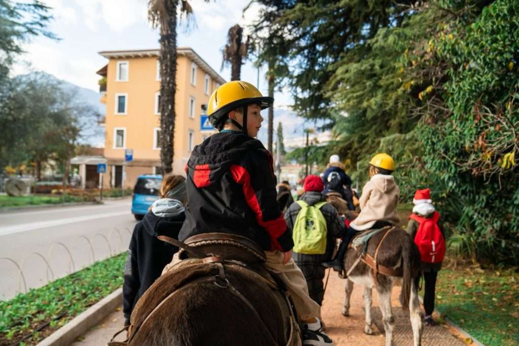 Niños con casco montando en burro por una avenida arbolada de Arco