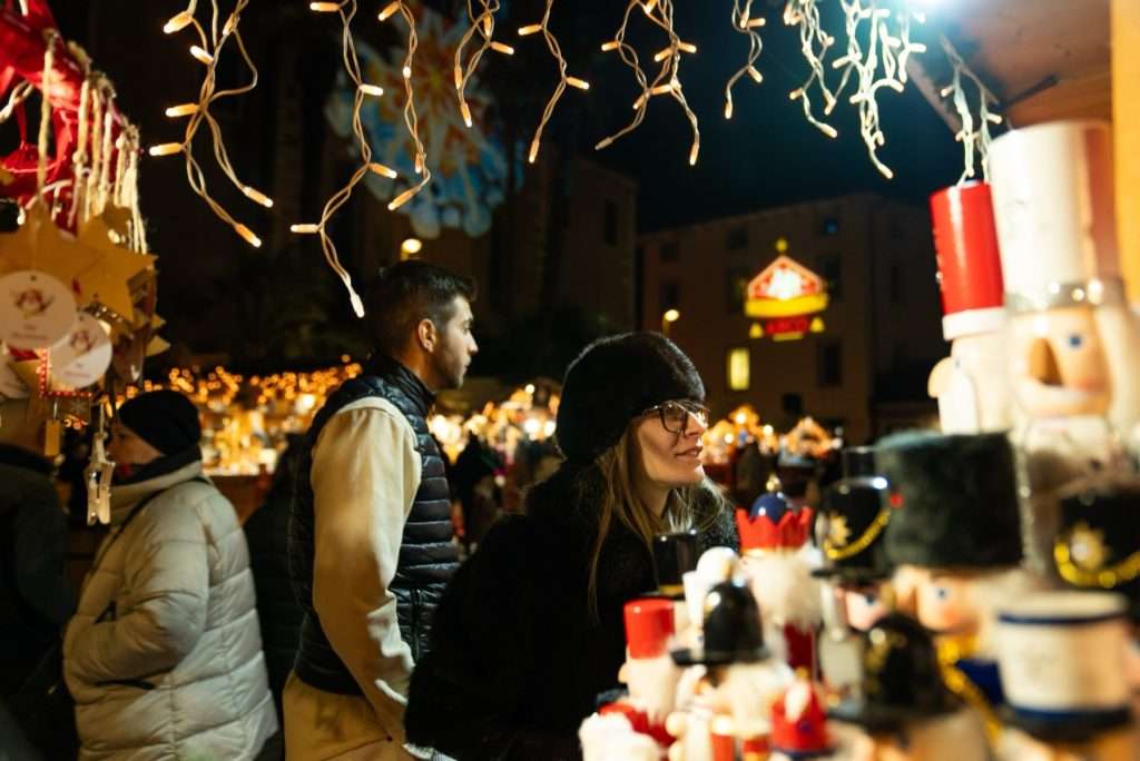 Visitantes ante un puesto de cascanueces de madera bajo las luces del mercadillo de Arco