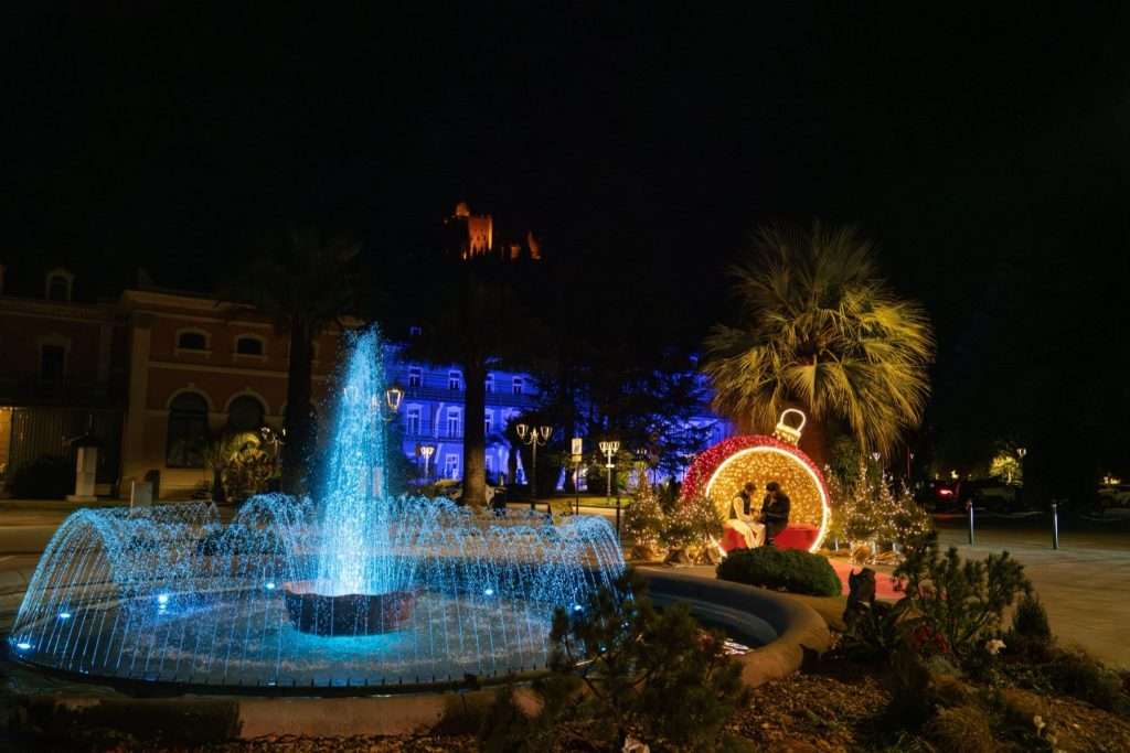 La fuente iluminada y una gran bola de Navidad, con el castillo de Arco iluminado al fondo